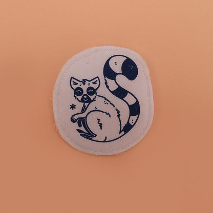 Broche mignonne fabriquée à la main avec des chutes de tissus. Dessin de lémurien à queue rayée.