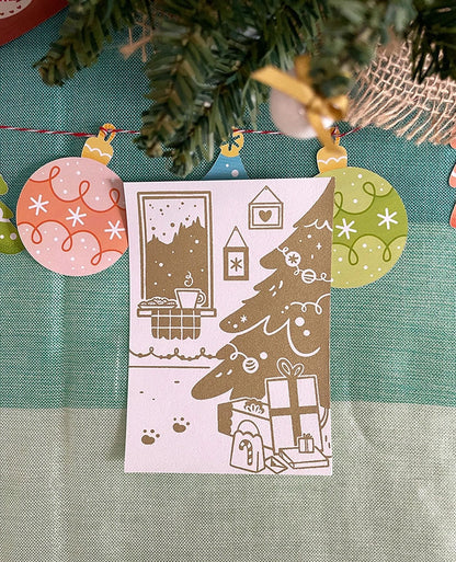 Carte de vœux sérigraphiée artisanalement. Décor cosy de fêtes. Cheminée, biscuits, chocolat chaud, sapin et cadeaux.