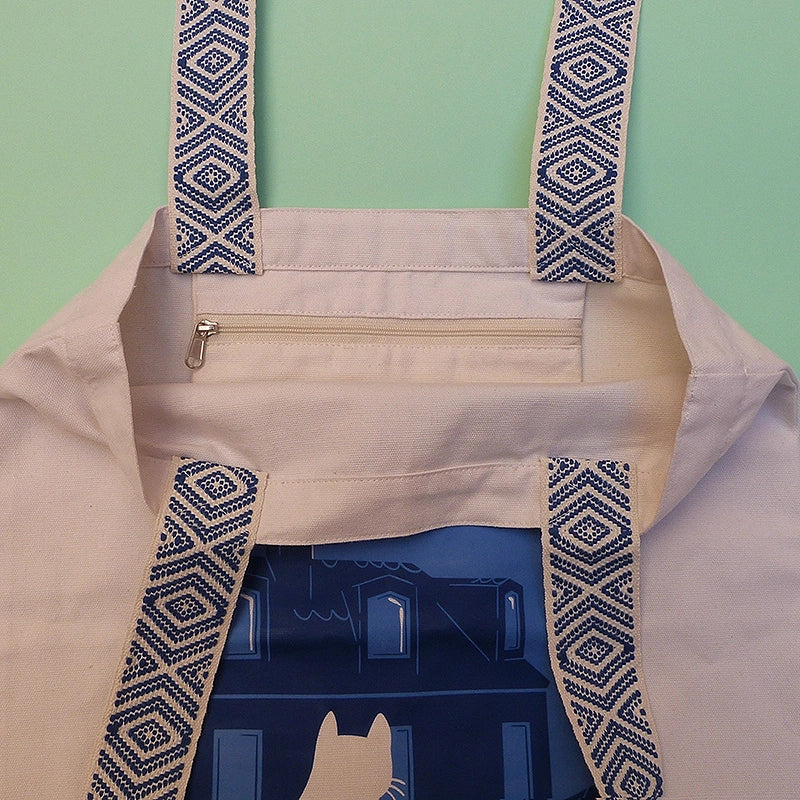 Grand totebag fabriqué en matières recyclées. Poche zippée à l'intérieur. Anses larges et confortables. Impression française. Illustration d'un chat regardant les toits de Paris la nuit.